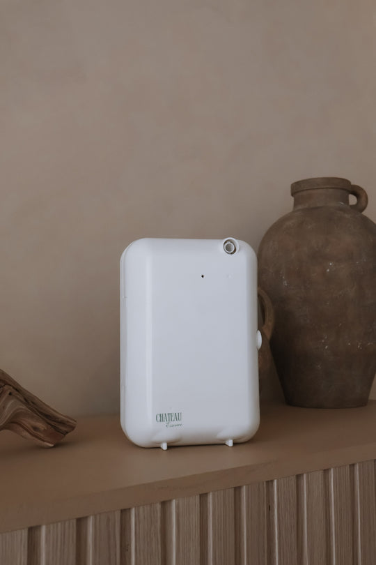 Chateau Air Luxury Diffuser and Cold-Air Scent System displayed on a modern wooden shelf beside decorative vases, showcasing elegant white design and hotel-quality aroma diffusion by Chateau Essence