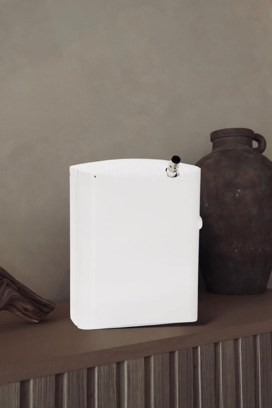 Prestige Luxury HVAC Diffuser and Cold-Air Scent System displayed on a wooden surface beside ceramic decor, showcasing its elegant white design by Chateau Essence